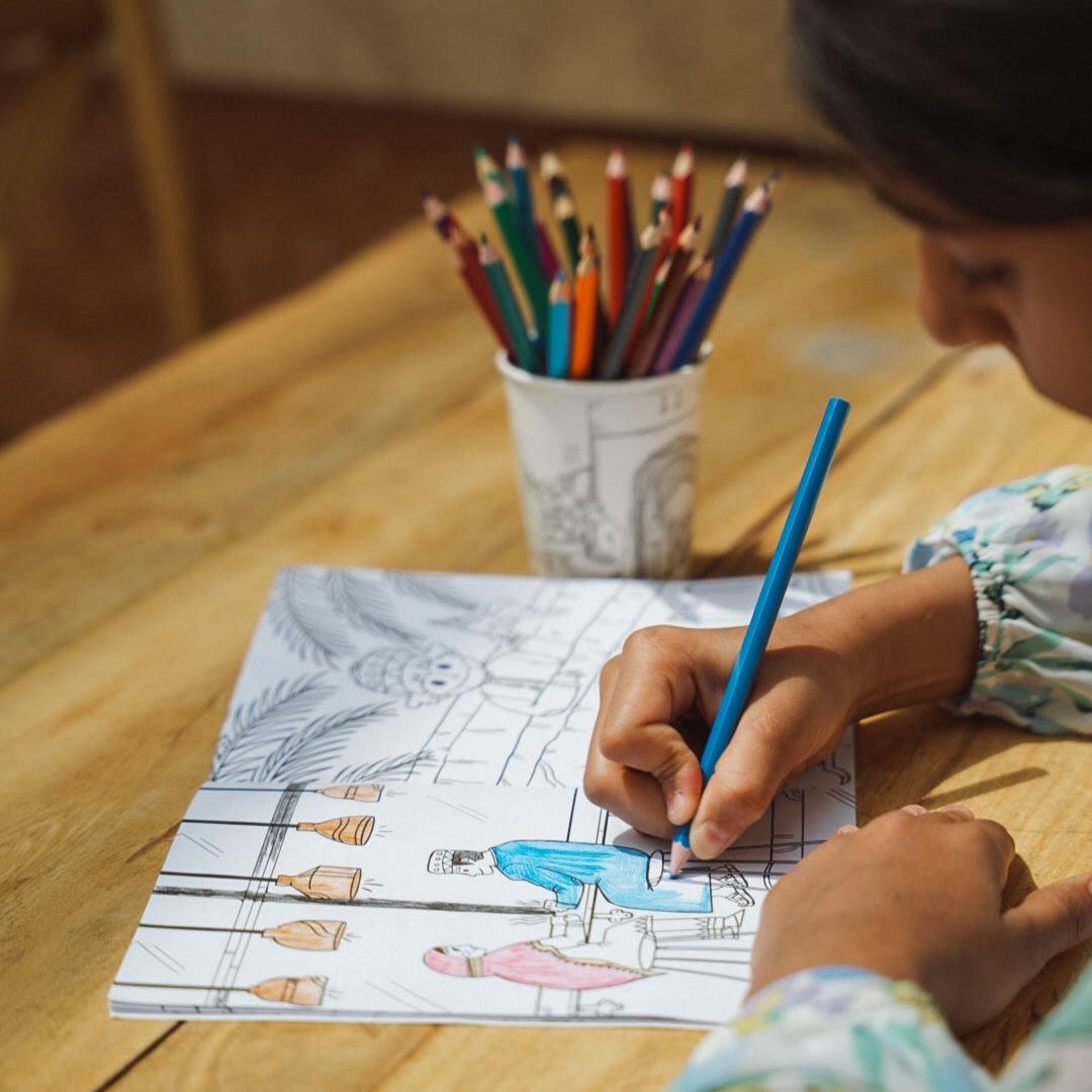 Child coloring a picture with colored pencils on a wooden table.