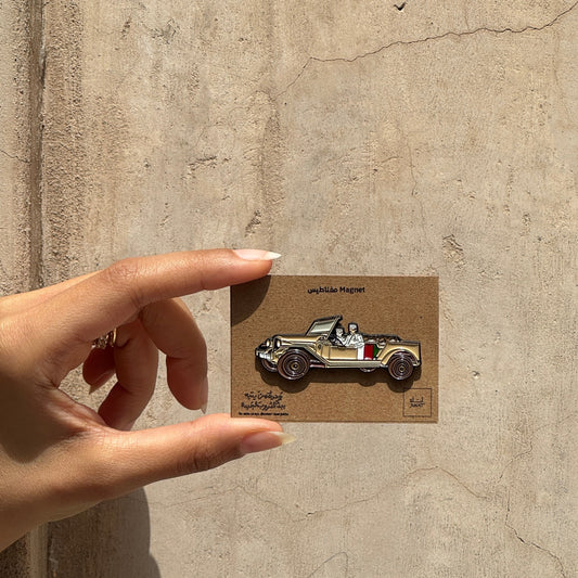 Hand holding a small card with a vintage car illustration against a textured wall.