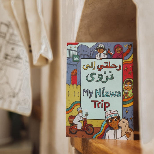 Colorful children's book titled 'My Nizwa Trip' on a wooden shelf with clothing in the background.